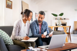 A couple reviewing receipts and taking notes while using a laptop in a cozy living room.