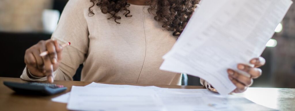 A person making financial decisions, holding documents in one hand and using a calculator with the other.